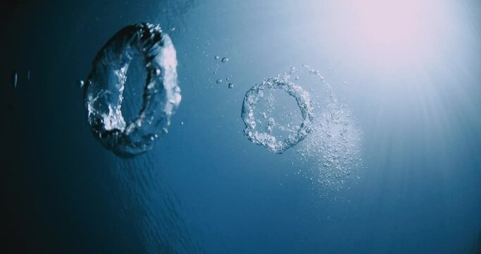 Ring bubbles underwater and sun rays in transparent blue ocean.