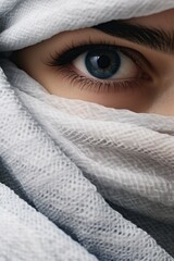 Close-up of a woman's eye over a white scarf on her face