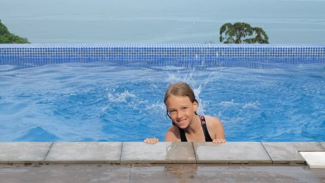 Little girl enjoying vacation in infinity pool, dangling feet in water, slow motion. Summer vacation and travel concept