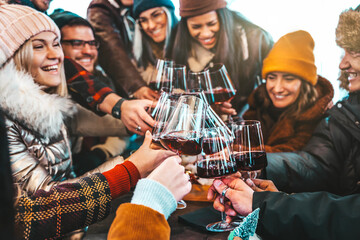 Fototapeta na wymiar Happy multiracial friends toasting red wine at restaurant terrace - Group of young people wearing winter clothes having fun at outdoors winebar table - Dining life style and friendship concept