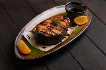 Grilled salmon steak on plate with lemon, herbs and spices on dark wooden background. Close up.