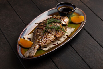 Grilled dorado with lemon and sauce on wooden table background. Bbq fish and vegetables. Roasted dorado with garnish.