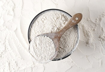 Wheat flour in wooden spoon and bowl background and texture, top view