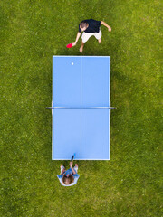 Aerial view people playing ping pong match outdoor. Top view two boys playing table tennis on a green grass lawn. Aerial view outdoor sport