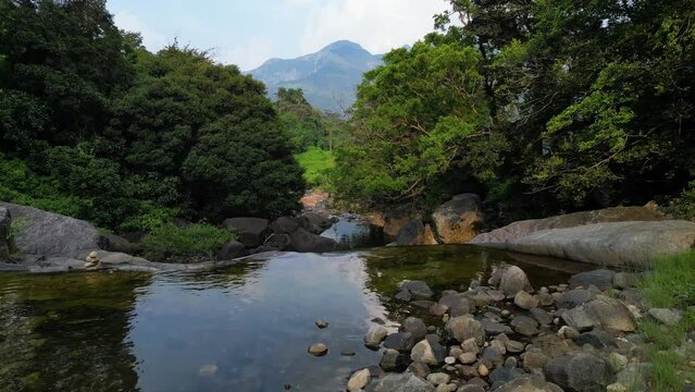Captivating aerial footage of a drone ascending from a waterfall-laden river nestled within a forested, rural mountainous village in the picturesque hill country.
