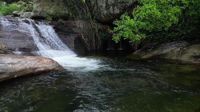 aerial footage as a drone gracefully hovers back from a picturesque waterfall nestled within a mountainous rural village, surrounded by lush forest