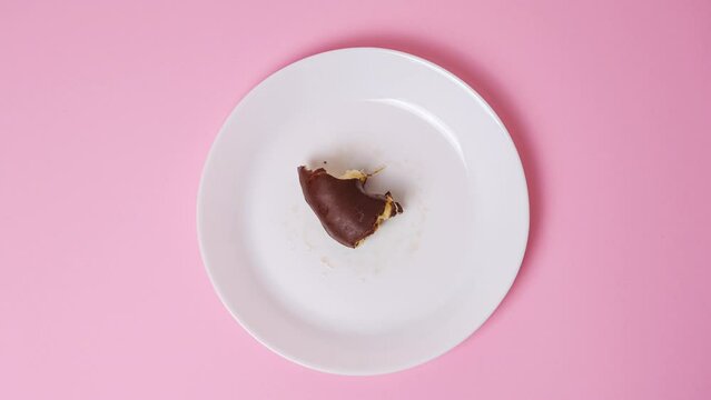 Eating delicious sweet donut covered with chocolate glaze on bright pink background. Stop motion food donut animation video. Bakery and food concept. Top view of chocolate doughnut in 4K.