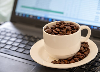 Cup of coffee that full of coffee beans on laptop background with rim light represents working...