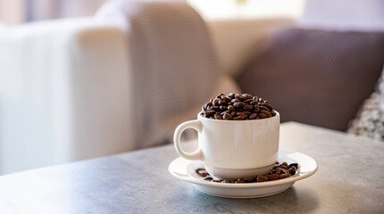 cup of coffee that full of coffee beans on grey living room table with couch background