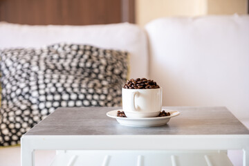 Cup of coffee on grey living room table with book and couch in the background