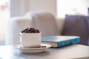 Cup of coffee on grey living room table with book and couch in the background