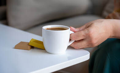 Old lady hand holding white cup of coffee with chocolate pieces