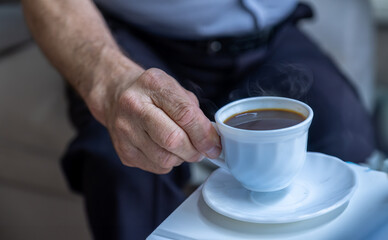 Old man hands holding cup of coffee on white table whearing shirts
