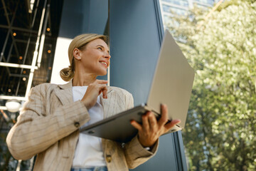 Bottom view of smiling woman manager working laptop on modern building background 