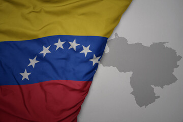 big waving national colorful flag and map of venezuela on the gray background.