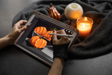 Girl's hand in special glove draws still life picture with pumpkins on electronic tablet near...
