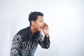 Young asian man wearing batik whispering and gossiping, side view isolated on white