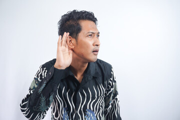 Asian man wearing batik eavesdropping with suspicious face in light studio