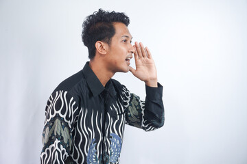 Young asian man wearing batik whispering and gossiping, side view isolated on white