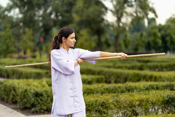 Young lady fighter with stick in hands wearing kimono training at the summer park alone