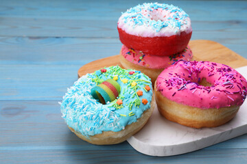 Sweet glazed donuts decorated with sprinkles on light blue wooden table, space for text. Tasty confectionery