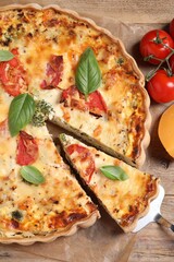 Tasty quiche with tomatoes, basil and cheese served on wooden table, flat lay