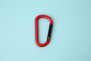 One red carabiner on light blue background, top view