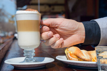Close-up of caucasian male hand holding mug of cappuccino on restaurant counter