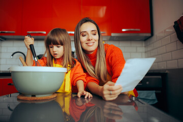 Mother Checking a Recipe While Cooking Next to her Daughter. Mom and daughter making traditional...