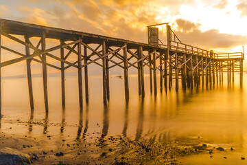 A wooden pier juts out into a calm body of water, bathed in the golden light of sunrise.