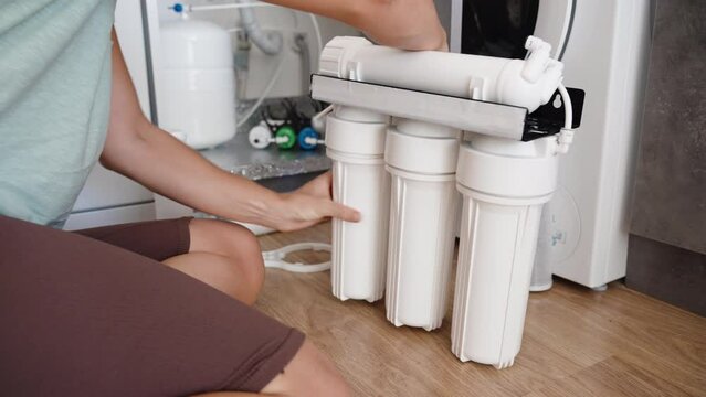 A young woman is changing the water filters for a reverse osmosis system in her kitchen by herself.
