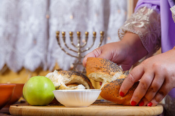 A woman's hand breaks the challah at the set table on the Jewish holiday Rosh Hashanah after prayer.