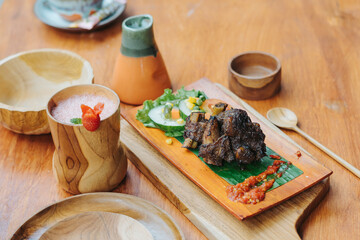 Indonesian food iga bakar or grilled ribs served on wooden plate with vegetable, sambal sauce, and strawberry juice