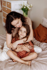 Happy loving family. Mother and her daughter girl play and hug while lying on the bed in a cozy bedroom.