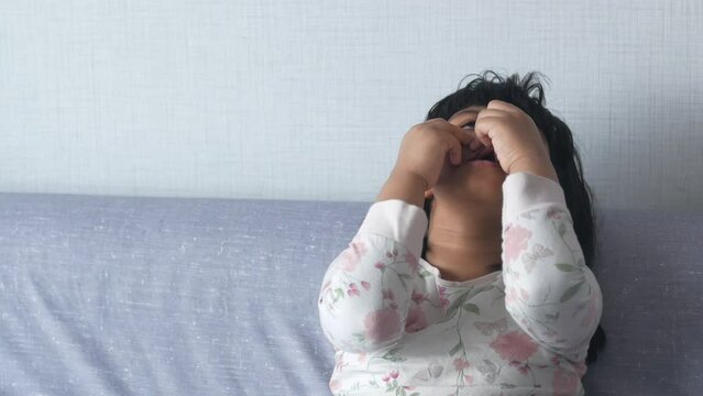 a upset crying child girl cover her face with hand sitting on sada 