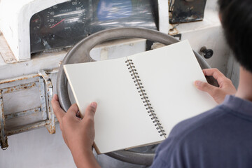 Closeup man holding blank notebook on car steering wheel,man opening blank notebook on inside car background,writing idea and taking note,concept of lifestyle and education ,copy space,sustainability.