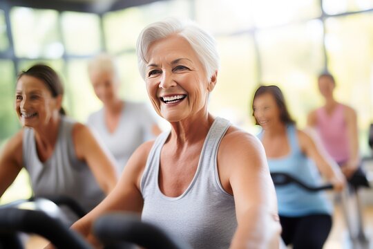 Group of women of different ages during cycling workout. Group fitness classes on exercise bikes. Workouts for any age. Be healthy in any age. Photo against a bright, gym studio background.