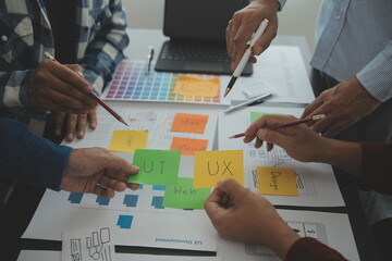 Close up ux developer and ui designer brainstorming about mobile app interface wireframe design on table with customer breif and color code at modern office.Creative digital development agency