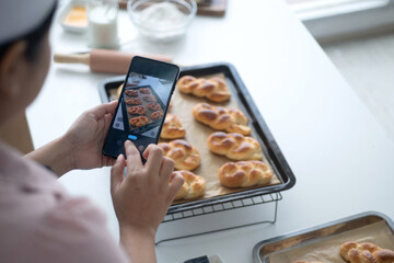 Female bakery chef or baker uses a with her smartphone mobile to take photos of freshly made bread...