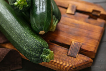 Brown board with many fresh zucchini on black wooden background