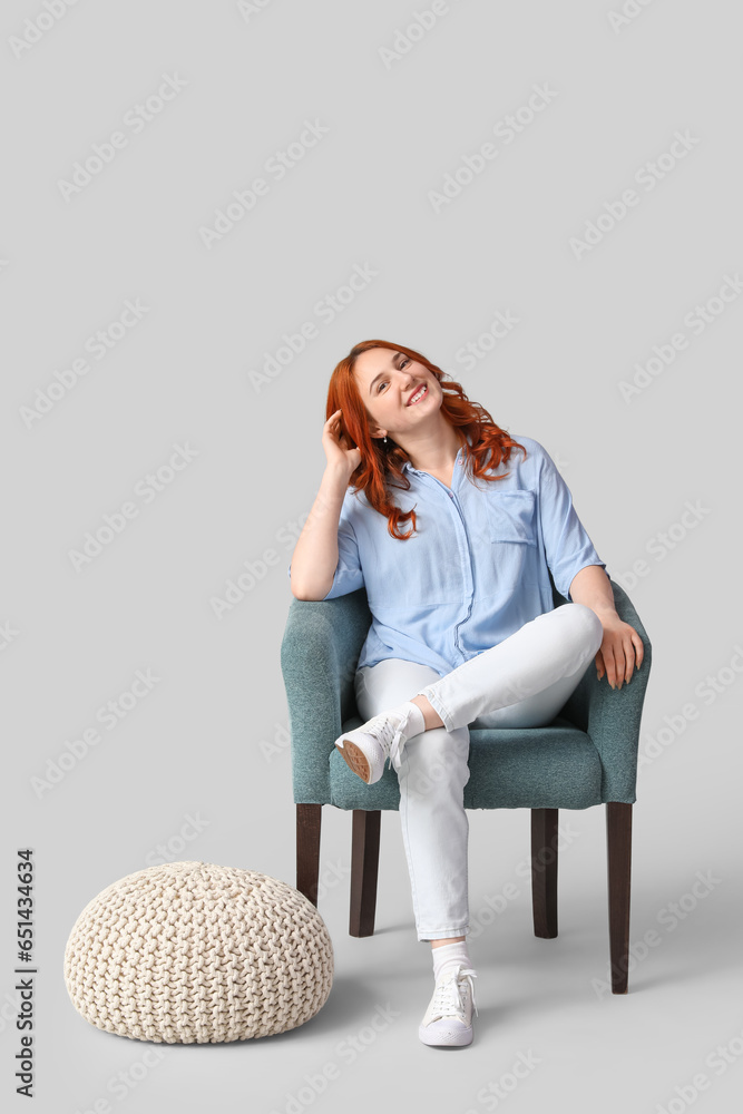 Poster Young woman sitting in soft armchair on light background