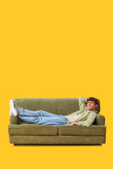 Young man resting on sofa against yellow background