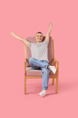 Happy young man sitting on chair against pink background