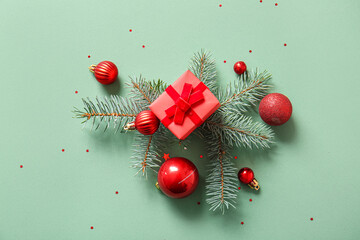 Christmas tree branches with balls and gift box on green background