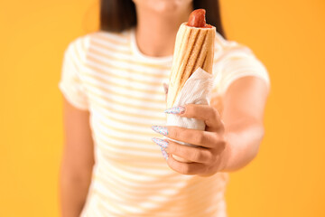 Young woman with tasty french hot dog on yellow background, closeup