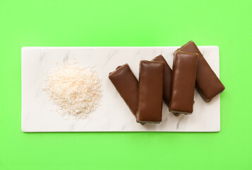 Board with tasty chocolate covered coconut candies on green background