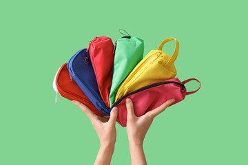 Female hands holding colorful pencil cases on green background