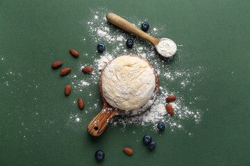 Composition with raw dough, almond and blueberry for preparing bakery on green background