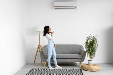 Beautiful Asian woman switching on air conditioner at home
