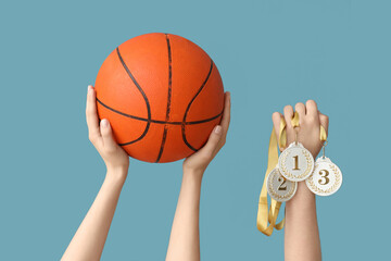 Female hands with basketball and medals on blue background